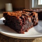 Close-up of a rich, fudgy slice of sweet potato brownies with visible chocolate chunks on a white plate.