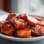 Close-up of thick, round slices of candied yams coated in a rich, dark brown glaze, served on a white plate.