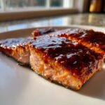 Close-up of a perfectly cooked salmon fillet generously topped with a thick, shiny, dark brown glaze.