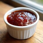 Close-up of thick, dark red homemade bbq sauce glistening in a small white ramekin.