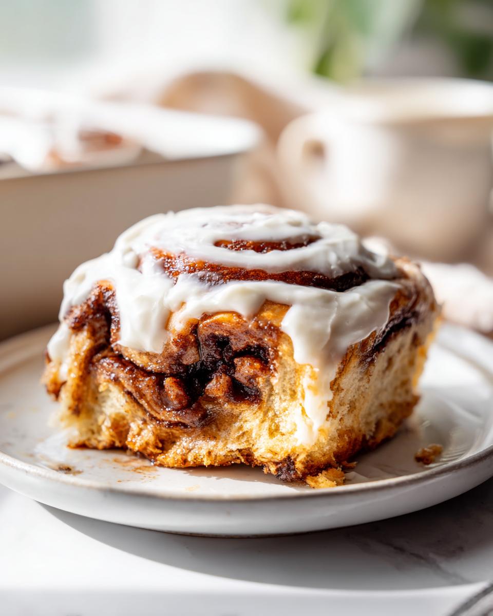 A close-up of a freshly baked cinnamon roll, generously topped with white icing, showing the gooey cinnamon swirl inside.