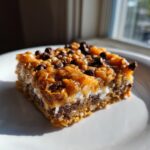 Close-up of a single, gooey slice of magic cookie bars showing seven distinct layers, topped with chocolate chips.