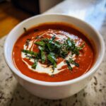 Close-up of a rich, creamy tomato bisque topped with a swirl of cream and fresh chiffonade basil.
