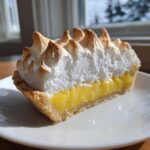 A perfect slice of lemon meringue pie showing bright yellow filling and toasted meringue peaks.