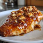 A close-up of a juicy chicken breast topped with a thick, glossy sauce and crumbled feta cheese, representing hot honey feta chicken.