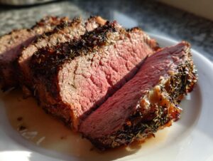 Close-up of several thick slices of a perfectly cooked rib roast showing a medium-rare pink center and herb crust.