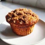 A single, golden brown oatmeal muffin topped with a thick layer of brown sugar streusel, sitting on a white plate.