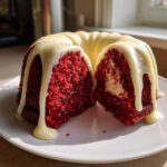 A moist red velvet bundt cake, cut in half to show the cream cheese center, drizzled with white glaze.