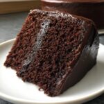 Close-up of a rich, moist slice of homemade chocolate cake covered in glossy chocolate frosting.