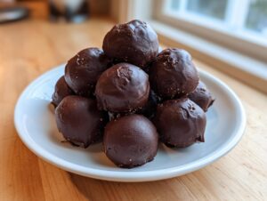 A stack of rich, chocolate-covered no-bake pecan pie balls served on a small white plate.
