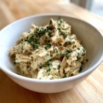 A white bowl filled with creamy, shredded slow cooker garlic parmesan chicken, topped generously with fresh parsley.