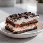 A perfect rectangular slice of 4-layer dirt cake showing alternating layers of dark cookie crust, chocolate mousse, and whipped cream, topped with cookie crumbs.