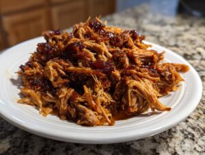 A close-up of shredded, saucy Slow Cooker Pulled Pork piled high on a white plate.