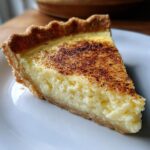 A close-up slice of smooth custard pie with a golden, nutmeg-dusted top and flaky crust.