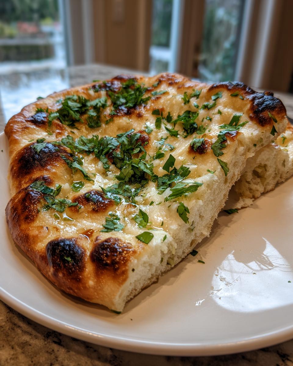 Close-up of a piece of soft, fluffy naan bread brushed with garlic butter and topped with fresh parsley.