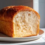 Close-up of a freshly baked sourdough sandwich bread loaf, showing the soft, airy interior crumb and golden crust.