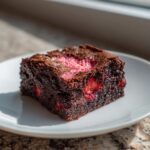 A rich, fudgy square of strawberry brownies featuring visible strawberry pieces and a pink center.