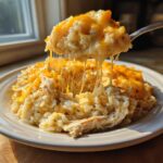 A spoonful of creamy cheesy chicken and rice lifted, showing long, gooey cheese pulls over the main dish.