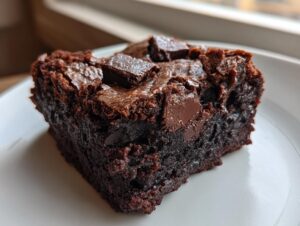 A close-up of a rich, dark square of sweet potato brownies topped with melted chocolate chunks on a white plate.