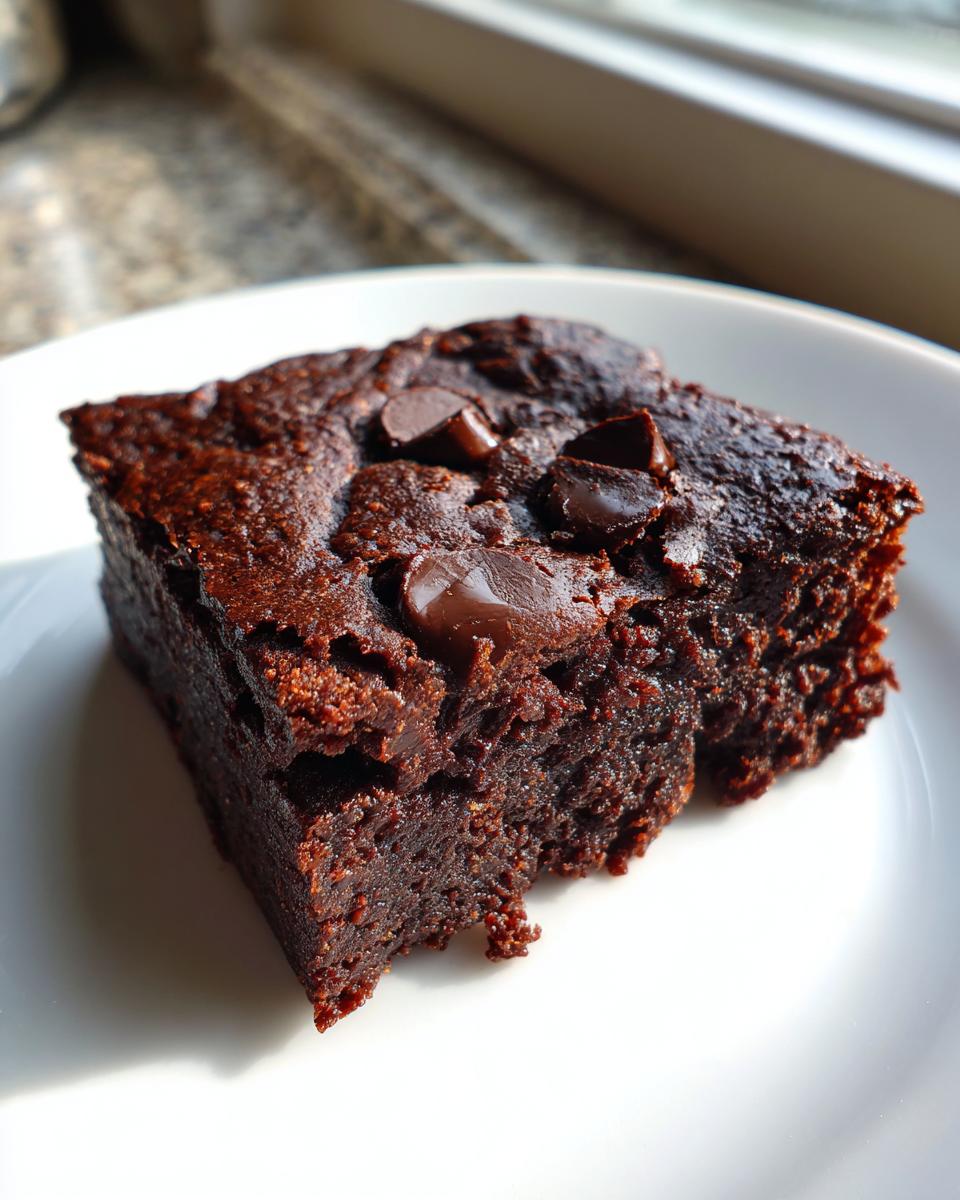 A rich, dark square slice of sweet potato brownies topped with melted chocolate chips on a white plate.