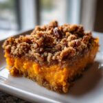 A rich, orange slice of sweet potato casserole topped with a thick, crunchy pecan streusel topping.