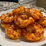 A close-up of cooked, seasoned air fryer frozen shrimp piled on a white plate.