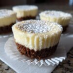 Close-up of a delicious mini cheesecake with a dark crust, topped with white powdered sugar.