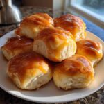 A stack of six fluffy, golden Texas Roadhouse rolls generously covered in melted honey butter glaze.