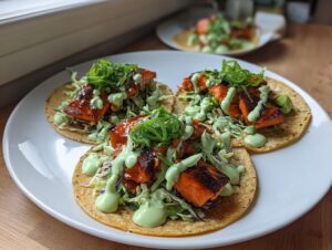 Three corn tortillas filled with blackened salmon chunks, slaw, and drizzled with a bright green creamy sauce, making perfect salmon tacos.