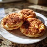 Three soft, round snickerdoodles generously coated in cinnamon sugar, resting on a white plate.