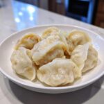 A white bowl filled with freshly steamed Traditional Chinese Dumplings resting on a marble countertop.