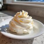 A beautiful, piped swirl of creamy vanilla buttercream frosting sitting on a small white plate.