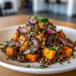 A serving of veggie lentil salad featuring brown lentils, roasted orange squash, and caramelized red onion, topped with parsley.