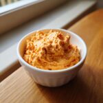A close-up of vibrant orange pumpkin fluff dessert or dip served in a small white bowl.
