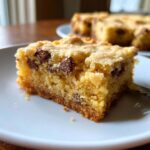 A close-up, tempting shot of a single square of soft, yellow cake mix cookie bars studded with chocolate chips on a white plate.