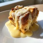 A close-up of a square serving of bread pudding drenched in thick vanilla sauce.