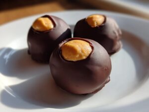 Close-up of three homemade peanut butter balls partially dipped in chocolate, showing the peanut butter center.
