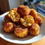 A pile of crispy, golden brown potato croquettes, with a few broken open showing the soft potato filling.