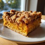 A close-up of a moist slice of pumpkin crunch cake topped with a thick, sugary, brown streusel topping.