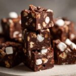 Close-up of stacked squares of rich chocolate rocky road fudge packed with marshmallows and nuts.