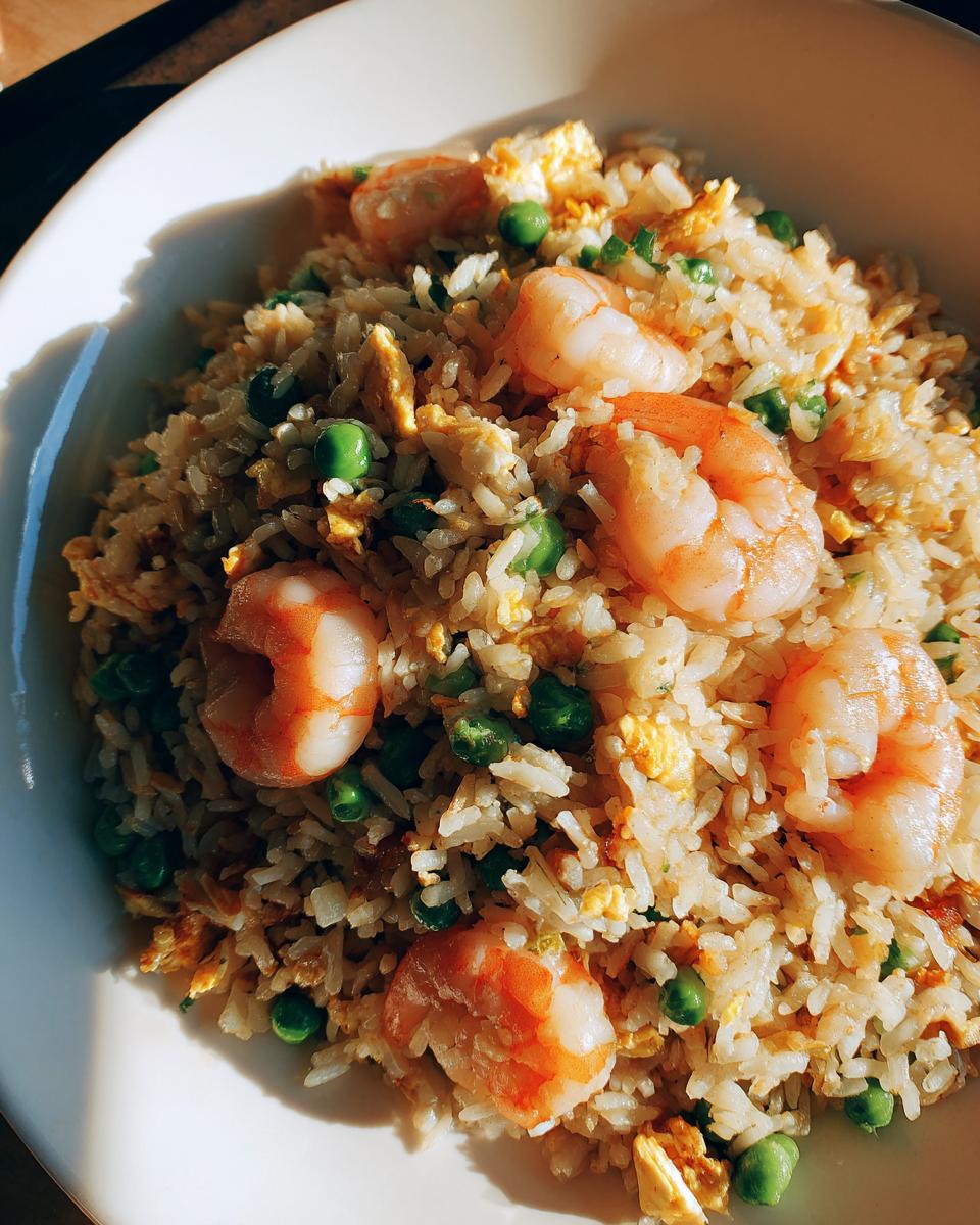 Close-up overhead shot of amazing shrimp fried rice with visible shrimp, peas, and scrambled egg in a white bowl.