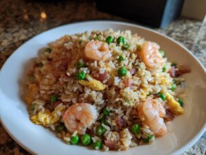 Close-up of delicious shrimp fried rice featuring plump shrimp, green peas, egg, and diced ham on a white plate.