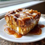 A close-up of a rich slice of apple bread pudding drenched in caramel sauce and drizzled with white icing.