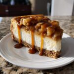 A decadent slice of apple pie cheesecake topped with spiced apples and dripping caramel sauce.