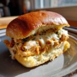 Close-up of a single buffalo chicken sliders sandwich with melted white cheese and parsley on a brioche bun.