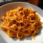 A close-up of creamy cajun chicken pasta featuring fettuccine noodles coated in a rich, orange-hued sauce with visible spices and chunks of chicken.