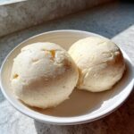 Two perfectly shaped scoops of smooth, pale cassava fufu served in a small white bowl, highlighted by natural sunlight.