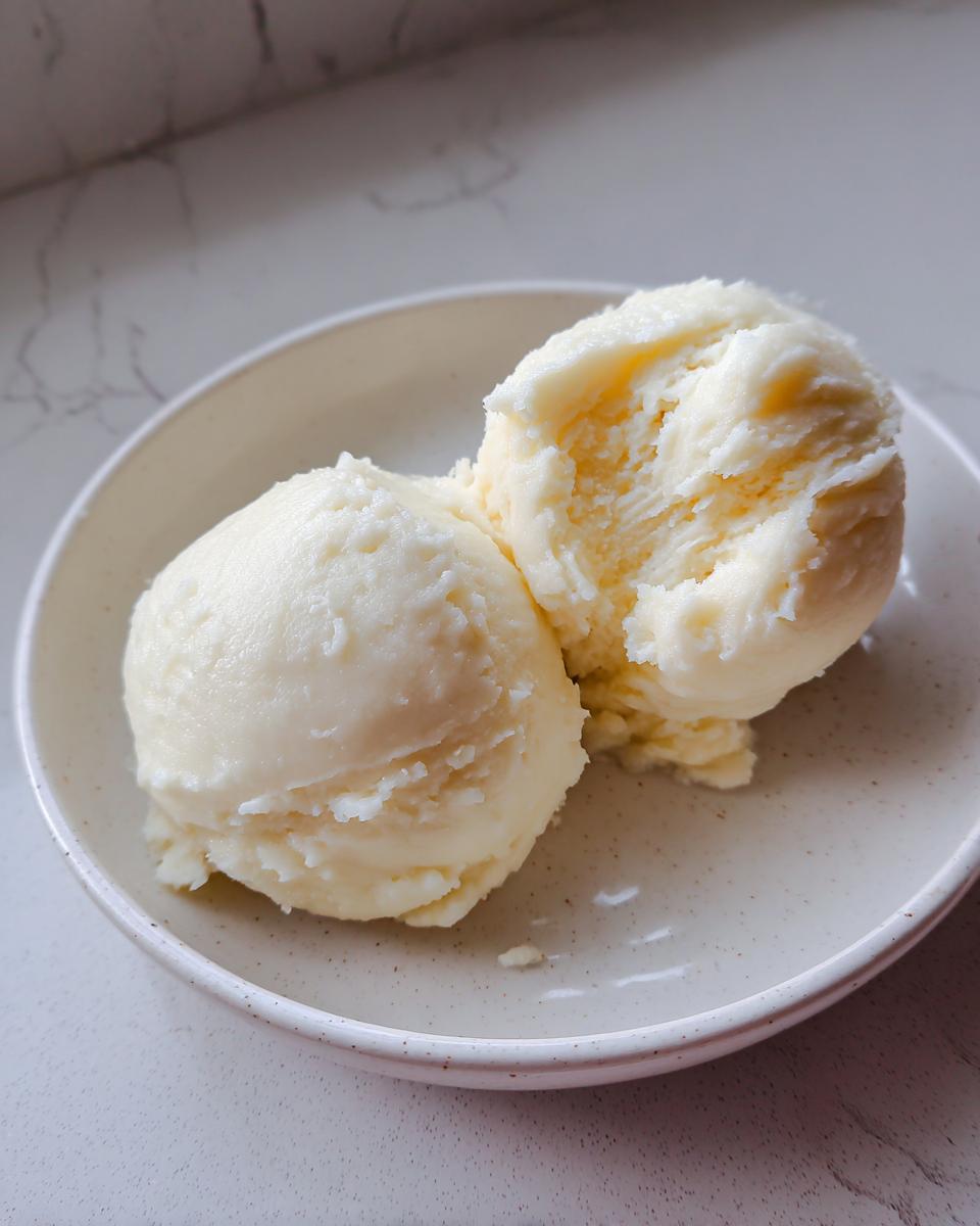 Two scoops of smooth, pale yellow cassava fufu served in a light speckled bowl.