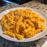A close-up of a generous serving of cheesy chicken pasta made with rotini noodles, coated in a rich orange sauce.