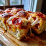 Close-up of freshly baked pizza sliders showing melted, stringy cheese and pepperoni on soft rolls.